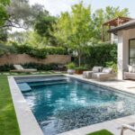 Moderner Pool mit hellen Beckenrandsteinen, umgeben von Naturstein, Grünpflanzen und gemütlicher Lounge-Ecke für eine luxuriöse Gartenatmosphäre.